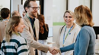 Vier Personen begrüßen sich auf einer Konferenz.