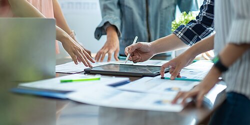 Vier Personen stehen um einen Tisch und arbeiten gemeinsam an einem Projekt.