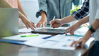 Vier Personen stehen um einen Tisch und arbeiten gemeinsam an einem Projekt.