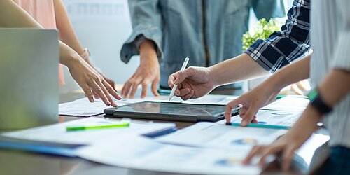 Vier Personen stehen um einen Tisch und arbeiten gemeinsam an einem Projekt.